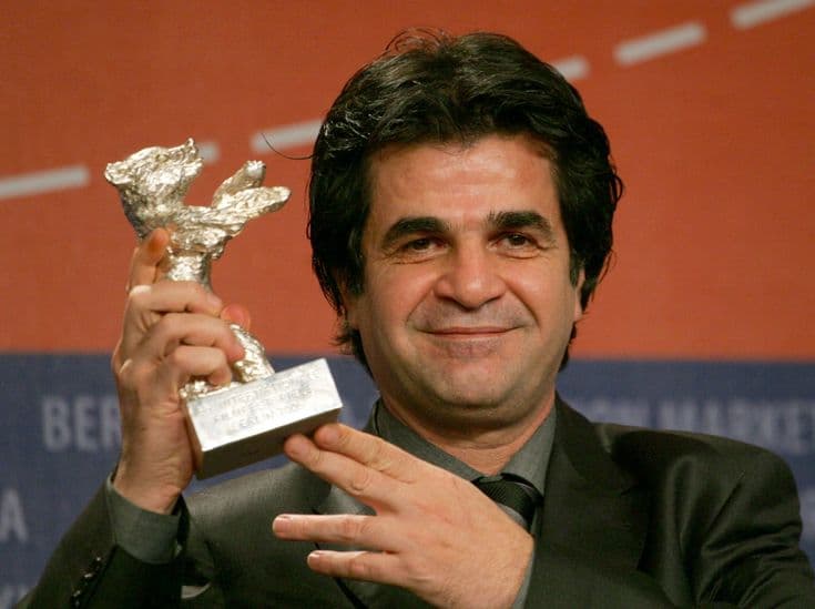 This may contain: a man holding up a silver trophy in front of a red wall