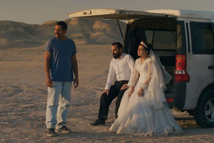This may contain: a man and woman standing next to a van in the desert
